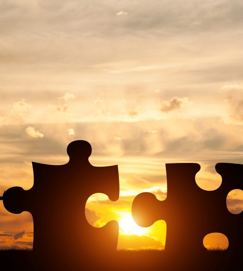 Two men connect two puzzle pieces. Sunset sky. Concept of business solution, teamwork, solving a problem, challenge